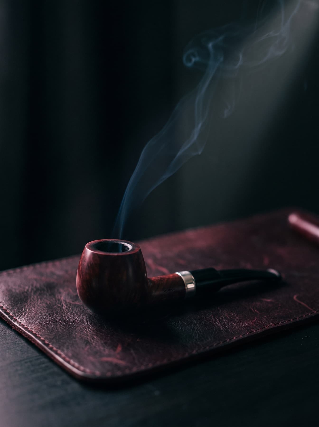 Koyu bordo deri üzerinde duran, gümüş bilezikli el yapımı funda kökü pipo ve yükselen ince duman